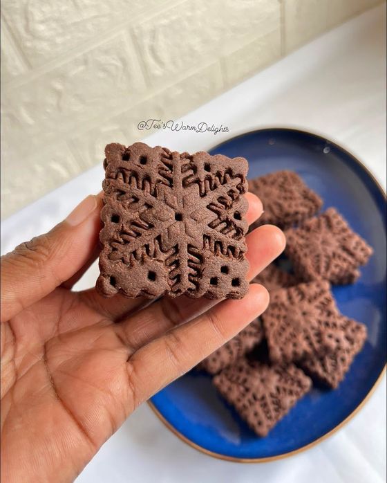 A hand holding a stamped chocolate biscuit above a blue plate.