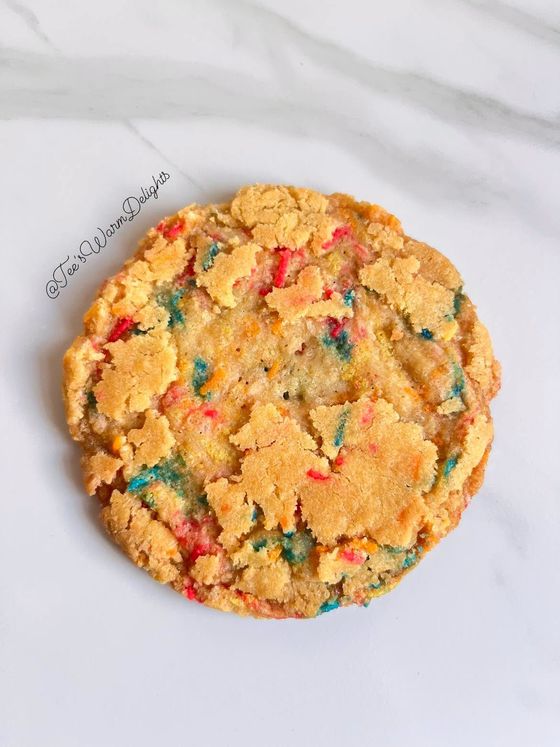 A golden funfetti cookie studded with coloured sprinkles.