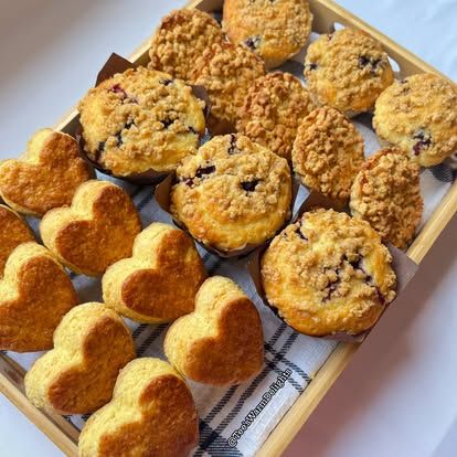 Heart-shaped scones and blueberry muffins on a wooden tray.