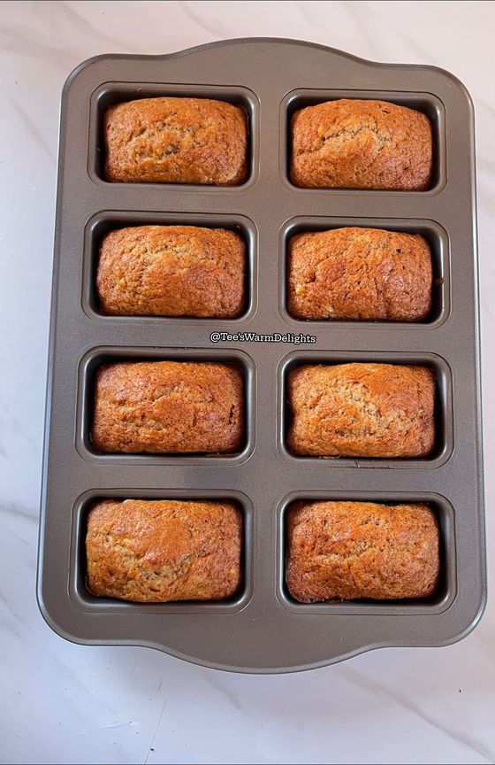 Eight mini loaves baking in a dark loaf tin.